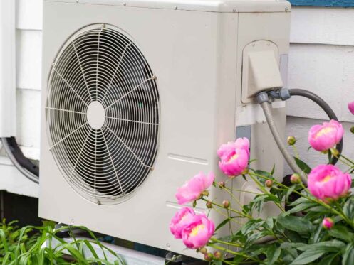 A heat pump outside a home with flowers around it